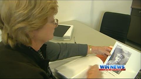 Screencap of a woman examining a black and white portrait of a soldier.