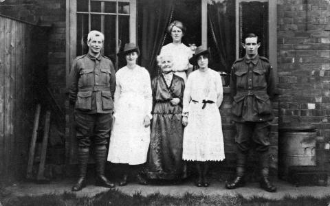 Black and white photograph of five people, three women two men. Men in uniform and women in white dresses.